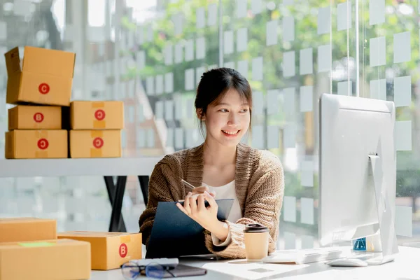 Woman who runs an e-commerce business is writing a list of customers on paper before shipping to them, she runs an e-commerce business on websites and social media. Concept of selling products online.