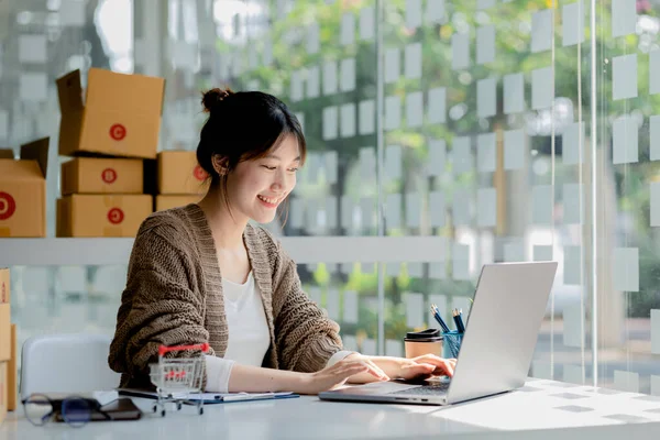 Güzel bir Asyalı işletme sahibi online bir dükkan açıyor, müşterilerin siparişlerini dizüstü bilgisayarla kontrol ediyor, malları bir kurye şirketi aracılığıyla gönderiyor, bir kadının online iş kurma kavramı.