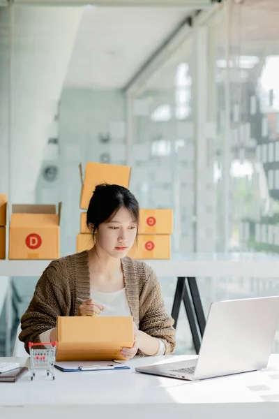 Woman who runs an e-commerce business is writing a list of customers on paper before shipping to them, she runs an e-commerce business on websites and social media. Concept of selling products online.