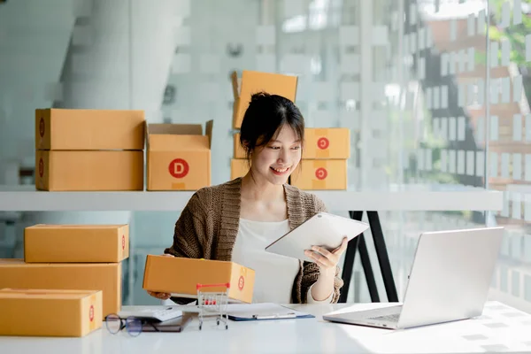 A beautiful Asian business owner opens an online store, she is checking orders from customers, sending goods through a courier company, concept of a woman opening an online business.
