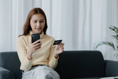 Oturma odasındaki kanepede akıllı telefon oynayan bir kadın, yoğun bir iş gününden sonra hafta sonları dinleniyor, internetten alışveriş yapıyor ve kredi kartıyla ödüyor. Kredi kartı ödeme kavramı.