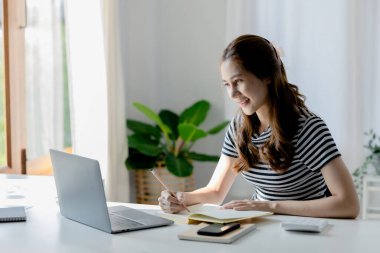 Bilgisayarda çalışan Asyalı bir kadın ve not defterine not alan bir üniversite öğrencisi, COVID-19 salgınından dolayı sınıfta bir salgını önlemek için online öğrenim kavramı..