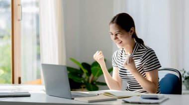 An Asian woman looks delighted after checking her exam results, she is a university student, The concept of online learning due to the COVID-19 outbreak to prevent an outbreak in the classroom.