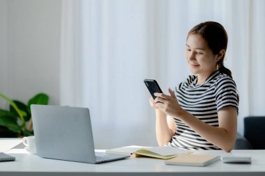 Kadın sınıf arkadaşlarına çevrimiçi mesaj göndermek için cep telefonuna basıyor. COVID-19 salgını nedeniyle internetten okuyan bir üniversite öğrencisi. Salgın konseptini azaltmayı çevrimiçi öğrenme.