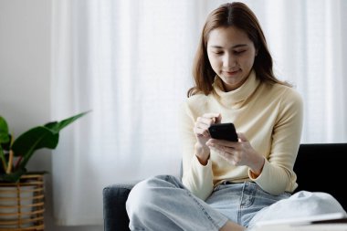 Oturma odasındaki kanepede akıllı telefon oynayan bir kadın, yoğun bir iş gününden sonra hafta sonları dinleniyor, internetten alışveriş yapıyor ve kredi kartıyla ödüyor. Kredi kartı ödeme kavramı.