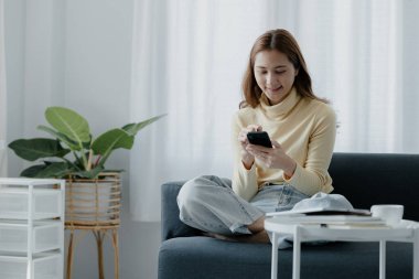 Oturma odasındaki kanepede akıllı telefon oynayan bir kadın, yoğun bir iş gününden sonra hafta sonları dinleniyor, internetten alışveriş yapıyor ve kredi kartıyla ödüyor. Kredi kartı ödeme kavramı.