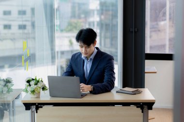 Asian man working in office at his company, Asian businessman checking on laptop in private office, executive room, young startup company executives. Management concept of startup company.