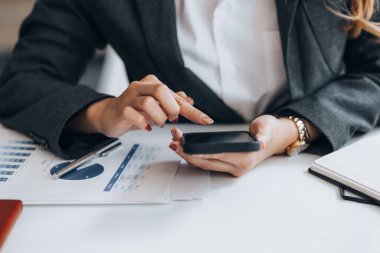 young businesswoman looking at financial information from a mobile phone, she is checking company financial documents, she is a female executive of a startup company. Concept of financial management.