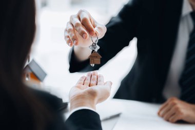 Bir ev kiralama şirketi çalışanı kira sözleşmesi imzalamayı kabul eden bir müşteriye kira sözleşmesinin detaylarını ve şartlarını açıklayan ev anahtarlarını teslim ediyor. Ev ve gayrimenkul kiralama fikirleri.