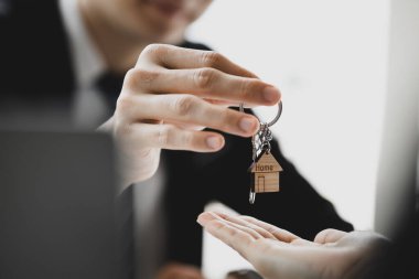 Bir ev kiralama şirketi çalışanı kira sözleşmesi imzalamayı kabul eden bir müşteriye kira sözleşmesinin detaylarını ve şartlarını açıklayan ev anahtarlarını teslim ediyor. Ev ve gayrimenkul kiralama fikirleri.