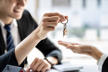 A home rental company employee is handing the house keys to a customer who has agreed to sign a rental contract, explaining the details and terms of the rental. Home and real estate rental ideas.