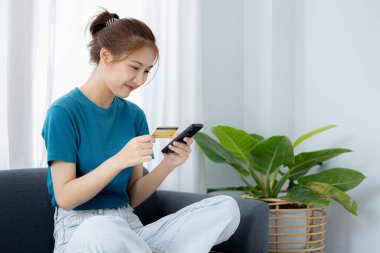 Oturma odasındaki kanepede akıllı telefon oynayan bir kadın, yoğun bir iş gününden sonra hafta sonları dinleniyor, internetten alışveriş yapıyor ve kredi kartıyla ödüyor. Kredi kartı ödeme kavramı.