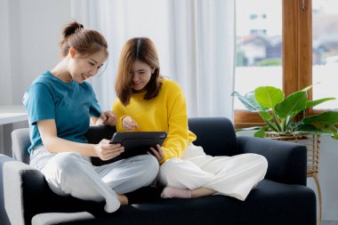 Oturma odasında iki kadın, online alışveriş için tabletlere göz atıyorlar, tatillerini birlikte film izleyerek ve müzik dinleyerek geçiriyorlar. Hafta sonu kaçamağı fikirleri.