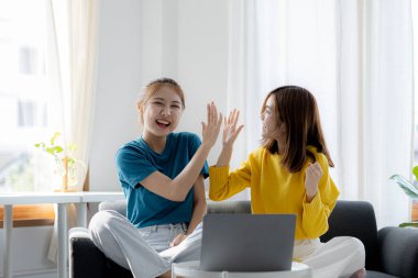 Oturma odasında COVID-19 salgını nedeniyle evden çalışan iki kadın, başarılı bir sunum ve online toplantı sonrasında sevinçlerini ifade etmek için ellerine dokundular. Ev kavramından çalış.