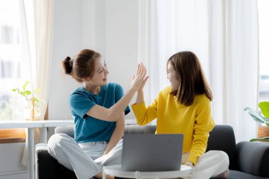 Oturma odasında COVID-19 salgını nedeniyle evden çalışan iki kadın, başarılı bir sunum ve online toplantı sonrasında sevinçlerini ifade etmek için ellerine dokundular. Ev kavramından çalış.