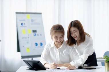 Girişim şirketinin atmosferinde, iki kadın çalışan, satışları artırmak ve yöneticilere raporlar hazırlamak için özetler ve pazarlama planları üzerinde çalışmak üzere fikir alışverişinde bulunuyorlar..