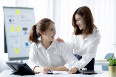 Girişim şirketinin atmosferinde, iki kadın çalışan, satışları artırmak ve yöneticilere raporlar hazırlamak için özetler ve pazarlama planları üzerinde çalışmak üzere fikir alışverişinde bulunuyorlar..