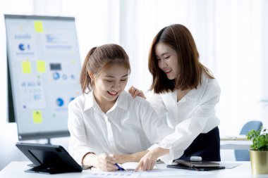 Girişim şirketinin atmosferinde, iki kadın çalışan, satışları artırmak ve yöneticilere raporlar hazırlamak için özetler ve pazarlama planları üzerinde çalışmak üzere fikir alışverişinde bulunuyorlar..