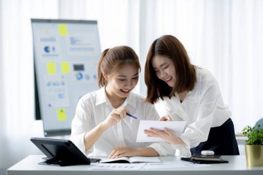 Girişim şirketinin atmosferinde, iki kadın çalışan, satışları artırmak ve yöneticilere raporlar hazırlamak için özetler ve pazarlama planları üzerinde çalışmak üzere fikir alışverişinde bulunuyorlar..