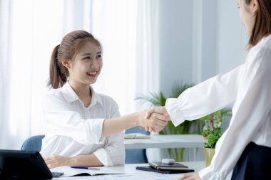 İki kadın el sıkışırken, iki iş kadını daha karlı büyüme yolları bulmak için beyin fırtınası ve pazarlama planlarını tartışmak üzere buluşurken el sıkışıyor. Karlı büyüme için işletme yönetimi fikirleri.