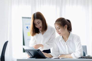 Girişim şirketinin atmosferinde, iki kadın çalışan, satışları artırmak ve yöneticilere raporlar hazırlamak için özetler ve pazarlama planları üzerinde çalışmak üzere fikir alışverişinde bulunuyorlar..