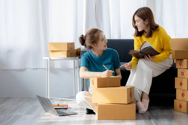 Two owners of an online store on the website are preparing parcels to send to customers following orders from the web page, they check the information and prepare for delivery to the customers.