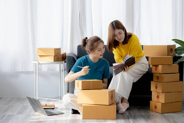 Two owners of an online store on the website are preparing parcels to send to customers following orders from the web page, they check the information and prepare for delivery to the customers.