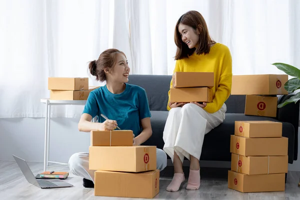 Two owners of an online store on the website are preparing parcels to send to customers following orders from the web page, they check the information and prepare for delivery to the customers.