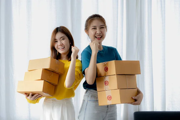 Two owners of an online store on the website are preparing parcels to send to customers following orders from the web page, they check the information and prepare for delivery to the customers.