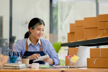 Güzel bir Asyalı işletme sahibi online bir dükkan açıyor, müşterilerin siparişlerini dizüstü bilgisayarla kontrol ediyor, malları bir kurye şirketi aracılığıyla gönderiyor, bir kadının online iş kurma kavramı.