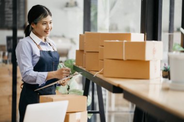 Bir çevrimiçi mağazanın sahibi, paketlenmiş ürünlerin siparişlerini web sitesinden sipariş edildiği gibi müşterilere teslimata hazırlamak için kontrol etmektedir. Çevrimiçi satış ve online alışveriş kavramları.