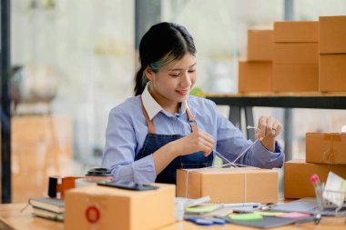 Paketi müşteri kutusuna bağlayan Asyalı bir kadın, çevrimiçi bir mağazası var, özel bir nakliye şirketi aracılığıyla paketleyip gönderiyor. Çevrimiçi satış ve online alışveriş kavramları.