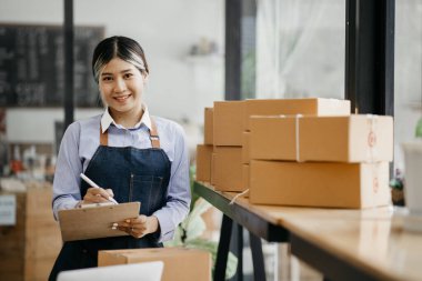 Bir çevrimiçi mağazanın sahibi, paketlenmiş ürünlerin siparişlerini web sitesinden sipariş edildiği gibi müşterilere teslimata hazırlamak için kontrol etmektedir. Çevrimiçi satış ve online alışveriş kavramları.