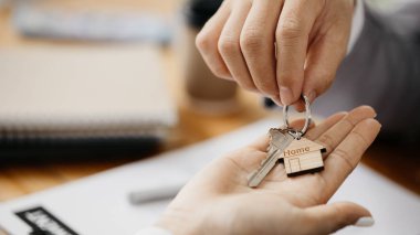 Bir ev kiralama şirketi çalışanı kira sözleşmesi imzalamayı kabul eden bir müşteriye kira sözleşmesinin detaylarını ve şartlarını açıklayan ev anahtarlarını teslim ediyor. Ev ve gayrimenkul kiralama fikirleri.