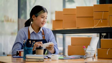  Güzel bir Asyalı işletme sahibi online bir dükkan açıyor, müşterilerin siparişlerini kontrol ediyor, bir kurye şirketi aracılığıyla mal gönderiyor, bir kadının online iş kurma kavramı.