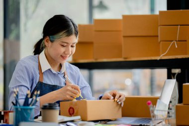  Güzel bir Asyalı işletme sahibi online bir dükkan açıyor, müşterilerin siparişlerini kontrol ediyor, bir kurye şirketi aracılığıyla mal gönderiyor, bir kadının online iş kurma kavramı.