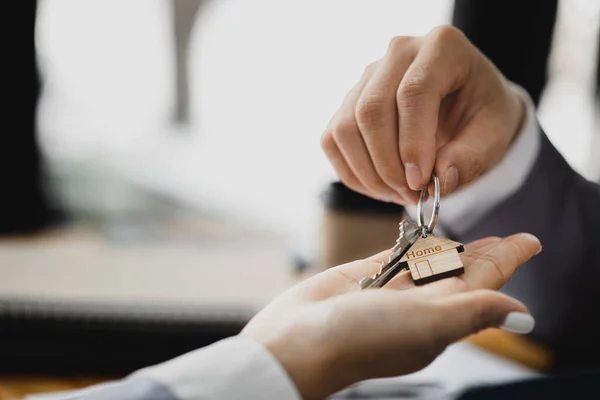 A home rental company employee is handing the house keys to a customer who has agreed to sign a rental contract, explaining the details and terms of the rental. Home and real estate rental ideas.