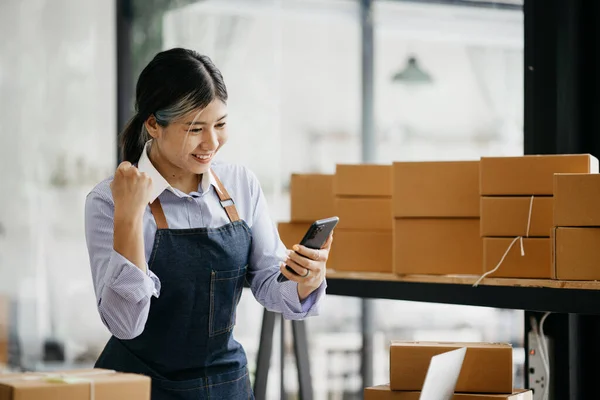 A beautiful Asian business owner opens an online store, she is checking orders from customers, sending goods through a courier company, concept of a woman opening an online business.