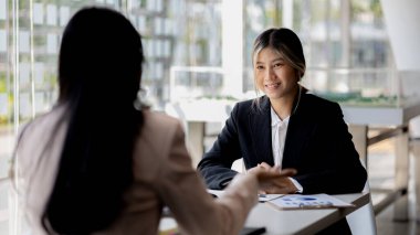 Girişim şirketinin atmosferinde, iki kadın çalışan, satışları artırmak ve yöneticilere raporlar hazırlamak için özetler ve pazarlama planları üzerinde çalışmak üzere fikir alışverişinde bulunuyorlar..