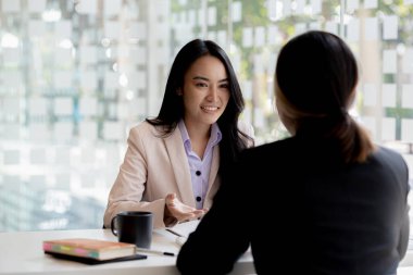 Girişim şirketinin atmosferinde, iki kadın çalışan, satışları artırmak ve yöneticilere raporlar hazırlamak için özetler ve pazarlama planları üzerinde çalışmak üzere fikir alışverişinde bulunuyorlar..