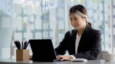 A beautiful Asian businesswoman sitting in her private office, she is checking company financial documents, she is a female executive of a startup company. Concept of financial management.