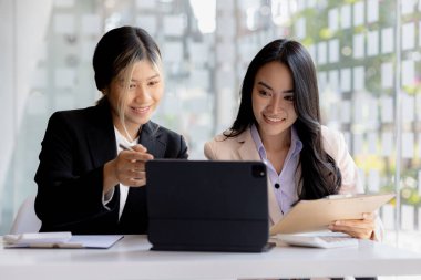 Girişim şirketinin atmosferinde, iki kadın çalışan, satışları artırmak ve yöneticilere raporlar hazırlamak için özetler ve pazarlama planları üzerinde çalışmak üzere fikir alışverişinde bulunuyorlar..