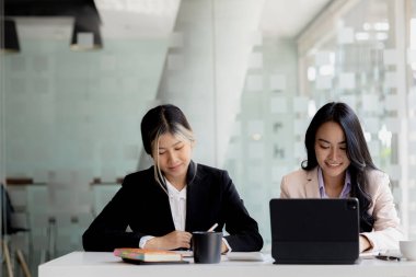 Girişim şirketinin atmosferinde, iki kadın çalışan, satışları artırmak ve yöneticilere raporlar hazırlamak için özetler ve pazarlama planları üzerinde çalışmak üzere fikir alışverişinde bulunuyorlar..
