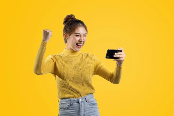 Portrait of a beautiful Asian woman in a yellow shirt playing on a smartphone. portrait concept used for advertisement and signage, isolated over the blank background, copy space.