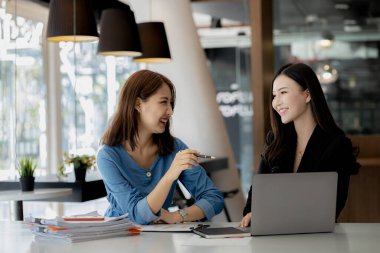 Girişim şirketinin atmosferinde, iki kadın çalışan, satışları artırmak ve yöneticilere raporlar hazırlamak için özetler ve pazarlama planları üzerinde çalışmak üzere fikir alışverişinde bulunuyorlar..