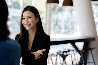 Girişim şirketinin atmosferinde, iki kadın çalışan, satışları artırmak ve yöneticilere raporlar hazırlamak için özetler ve pazarlama planları üzerinde çalışmak üzere fikir alışverişinde bulunuyorlar..