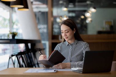 A beautiful Asian businesswoman sitting in her private office, she is checking company financial documents, she is a female executive of a startup company. Concept of financial management.