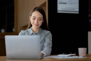Güzel Asyalı genç bir kadın dizüstü bilgisayardan bilgilere bakıyor. Asyalı iş kadınının konsept görüntüsü. Zeki, modern kadın yönetici, girişimci iş kadını, iş kadını..
