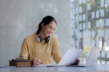 İnternette çalışmak için dizüstü bilgisayar kullanan güzel bir Asyalı kadın, çevrimiçi çalışıyor. Sınıfta bir salgını önlemek için COVID-19 salgını nedeniyle çevrimiçi öğrenme kavramı.