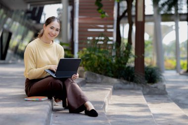 Üniversite binasının merdivenlerinde tablet kullanan Asyalı bir kadın, kız öğrenci, sınıfa giren kız öğrenci. Üniversite eğitimi kavramı.